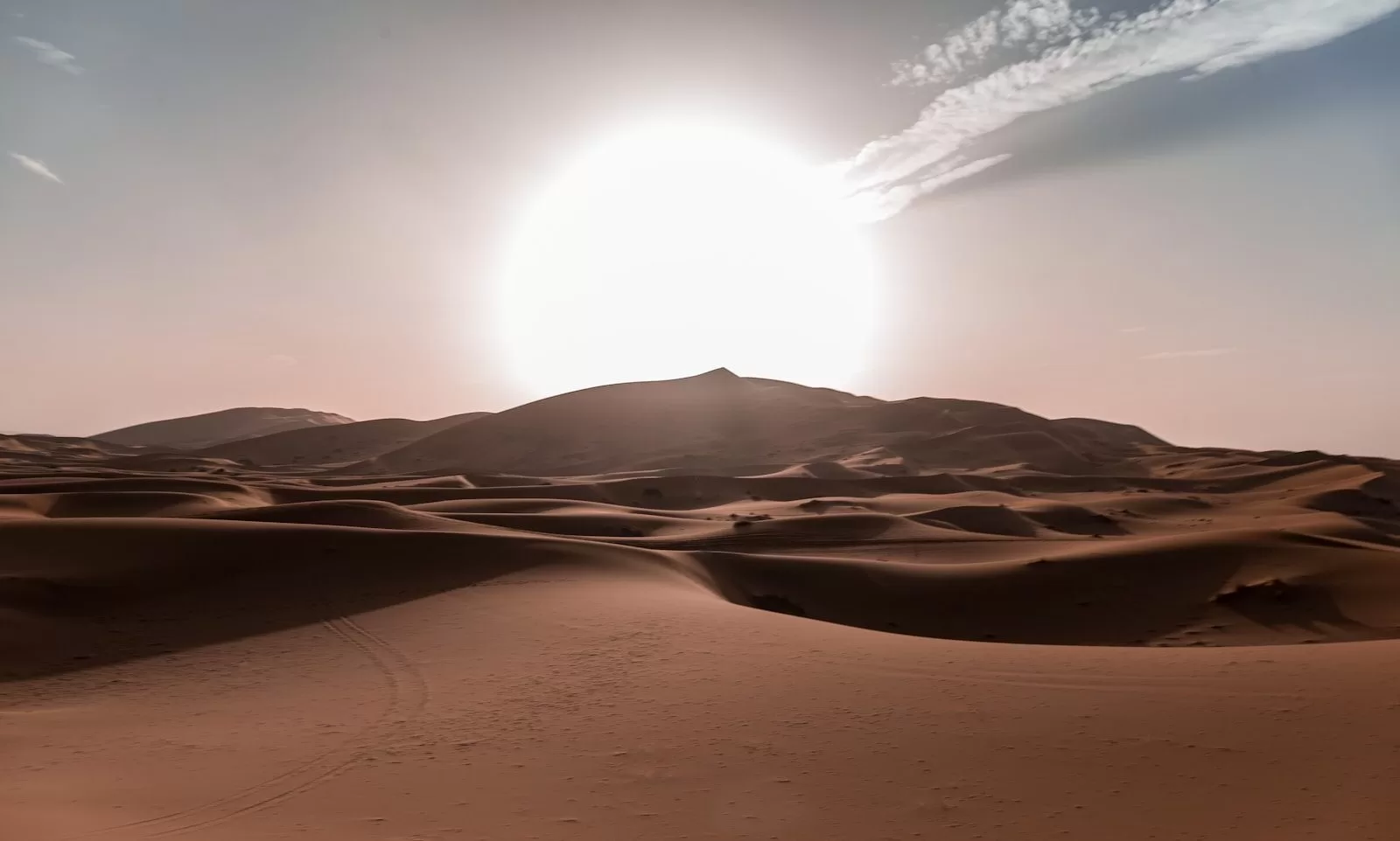 Sun rides over rolling sand dunes of the Sahara Desert